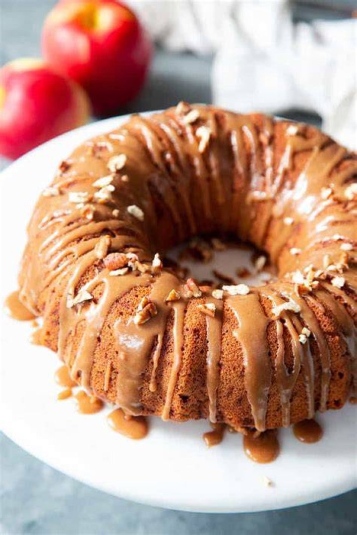 Apple bundt cake topped with cream cheese glaze on a white plate and a red striped napkin.